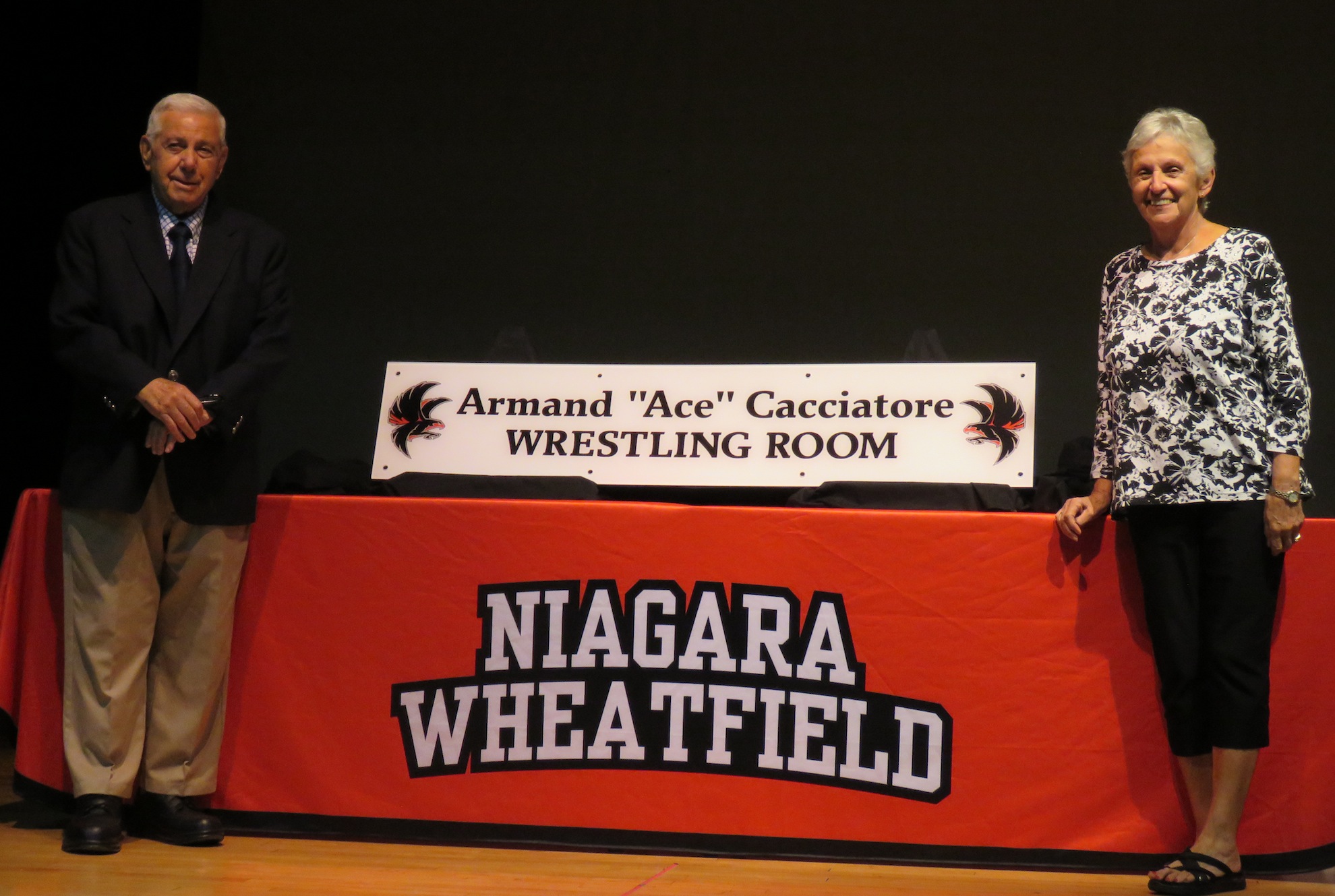 From left, Armand `Ace` Cacciatore and his wife, Mimi, pose with the new wrestling room sign dedicated in the coach's honor. (Photos by David Yarger)